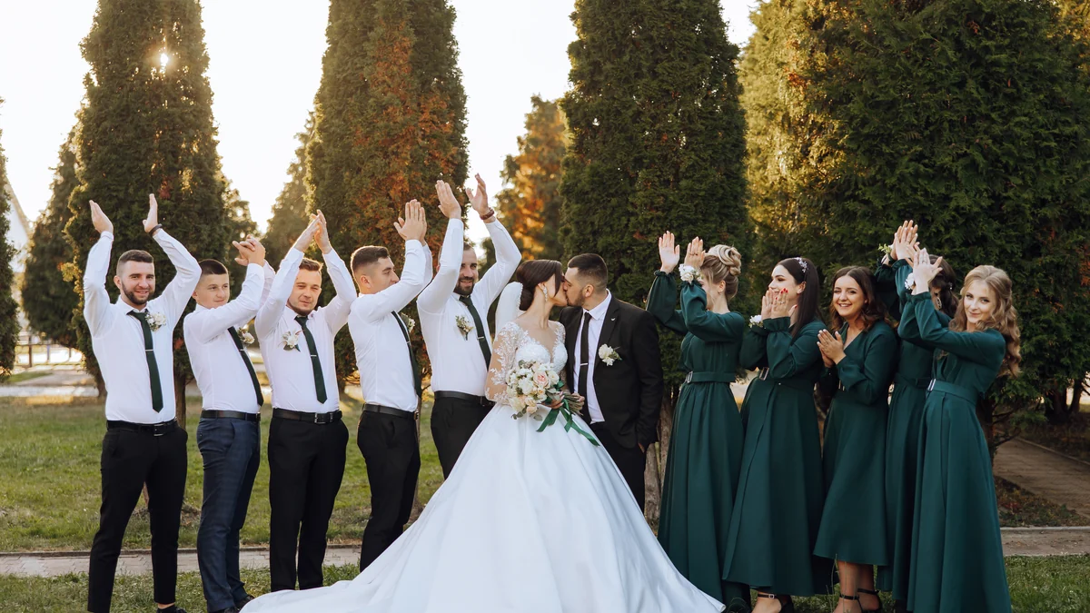 Wedding party in dark green bridesmaid dresses and shirtsleeves celebrating outdoors at golden hour