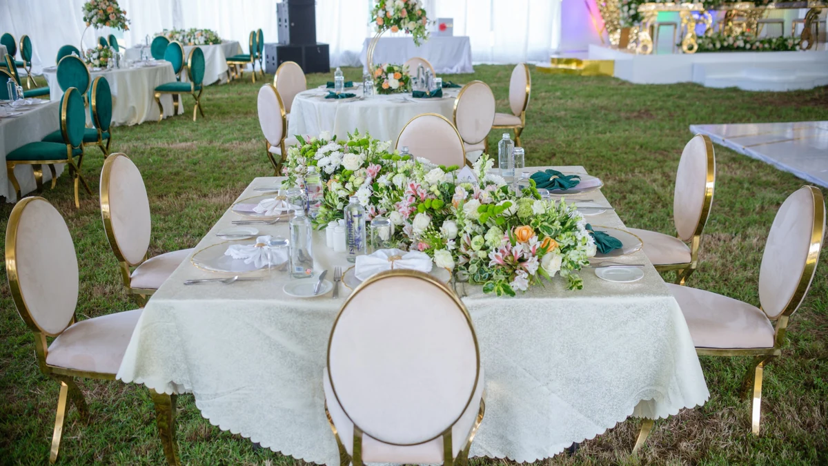 Long head table set with gold chairs, a floral runner and green napkins at a marquee reception