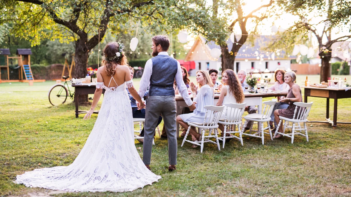 Bride and groom walking to a long table at an outdoor backyard wedding reception at sunset