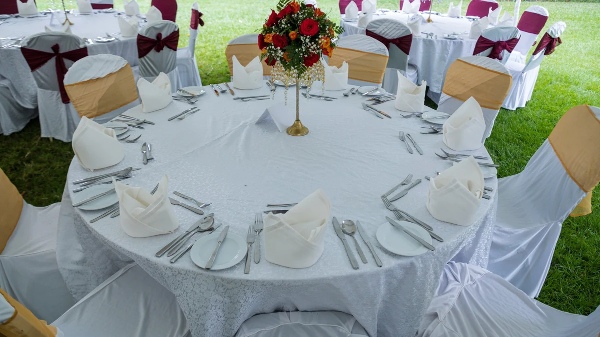 Round reception table laid for ten with white linen, folded napkins and a red and orange floral centerpiece