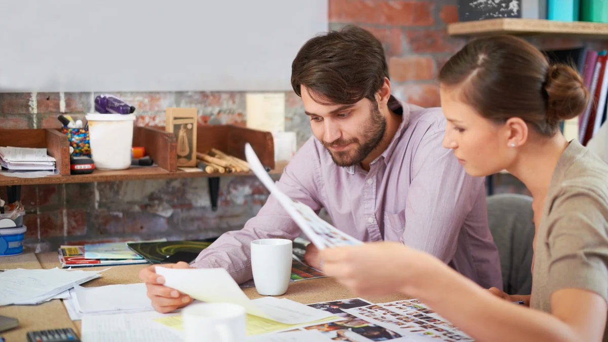 Two people reviewing printed design samples together at a desk scattered with proofs