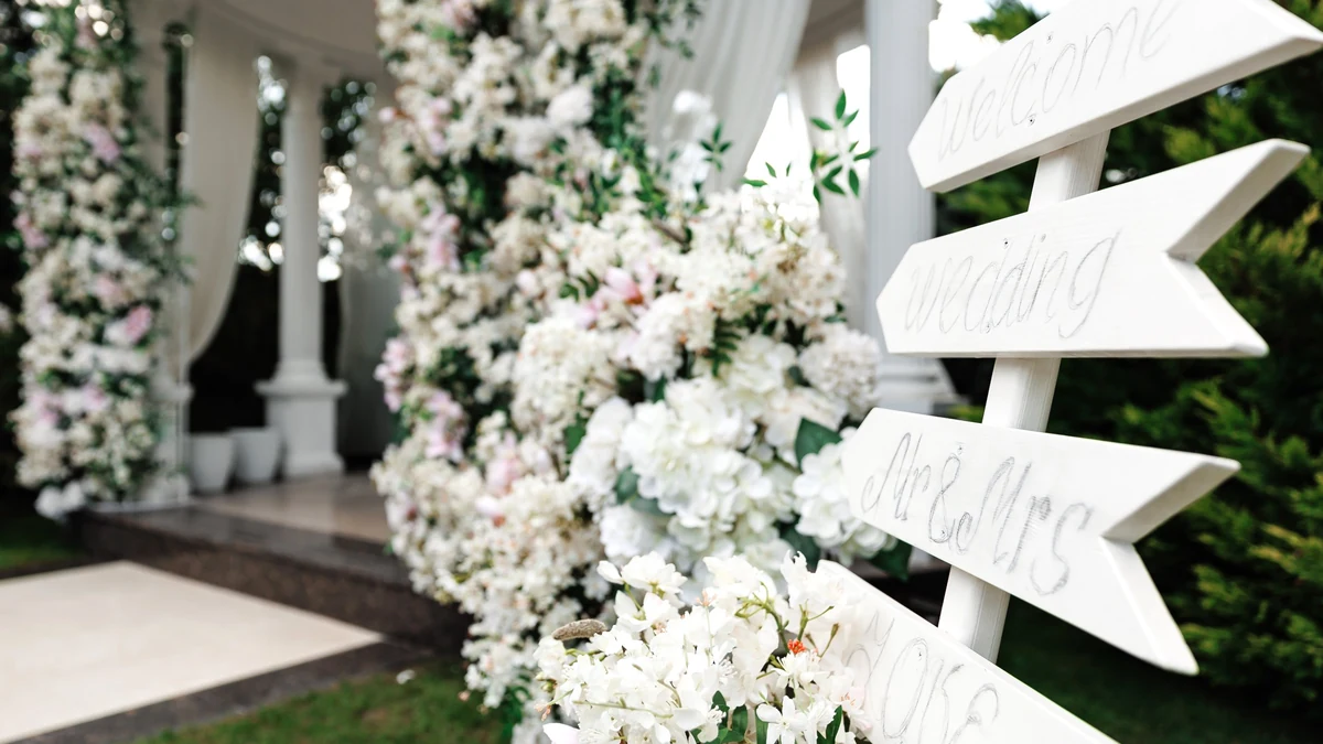White wooden directional signs reading welcome, wedding and Mr and Mrs beside white florals at a venue entrance