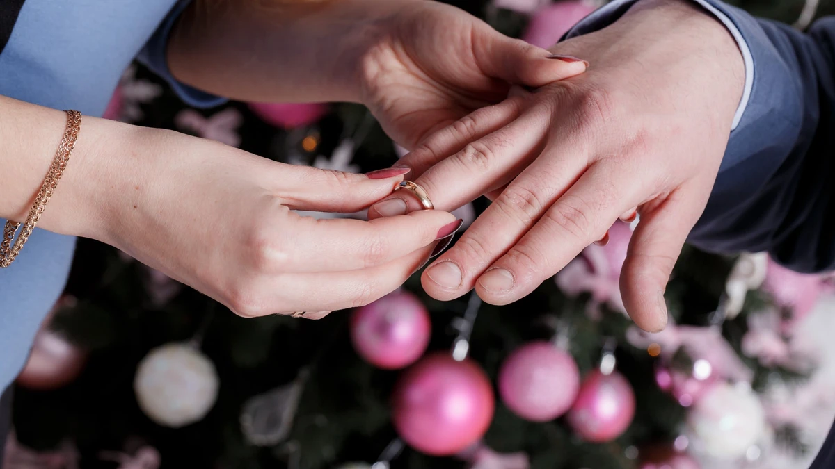 Close-up of a woman sliding a gold band onto a man’s ring finger