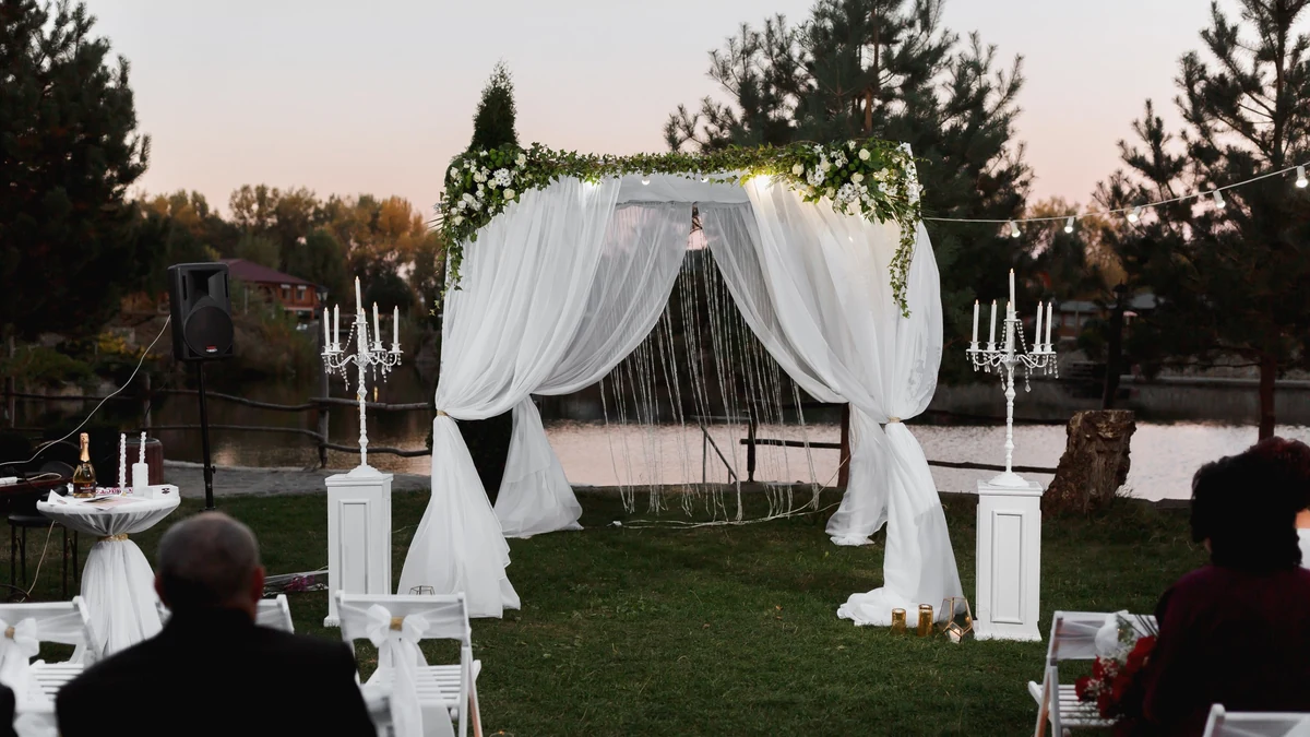 White draped four-post canopy decorated with greenery and candles at an outdoor lakeside wedding ceremony at sunset
