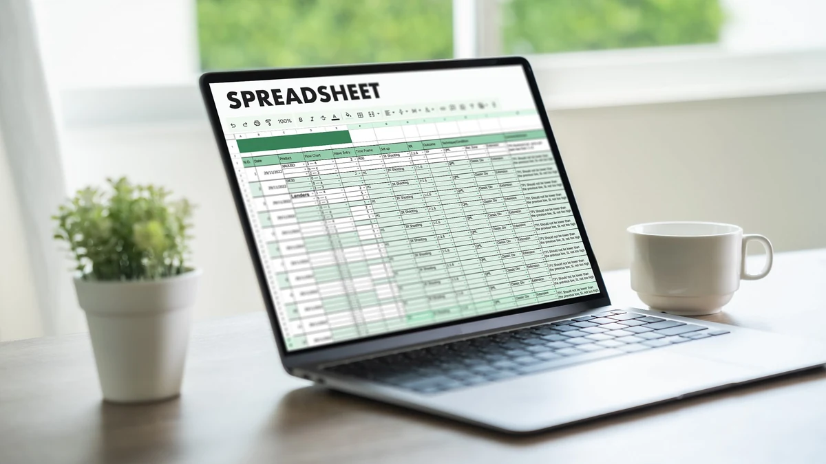 Open laptop displaying a spreadsheet on a desk beside a coffee cup and a small plant
