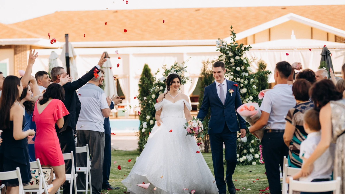 Newly married couple walking back up the aisle through falling rose petals as guests applaud during the wedding recessional