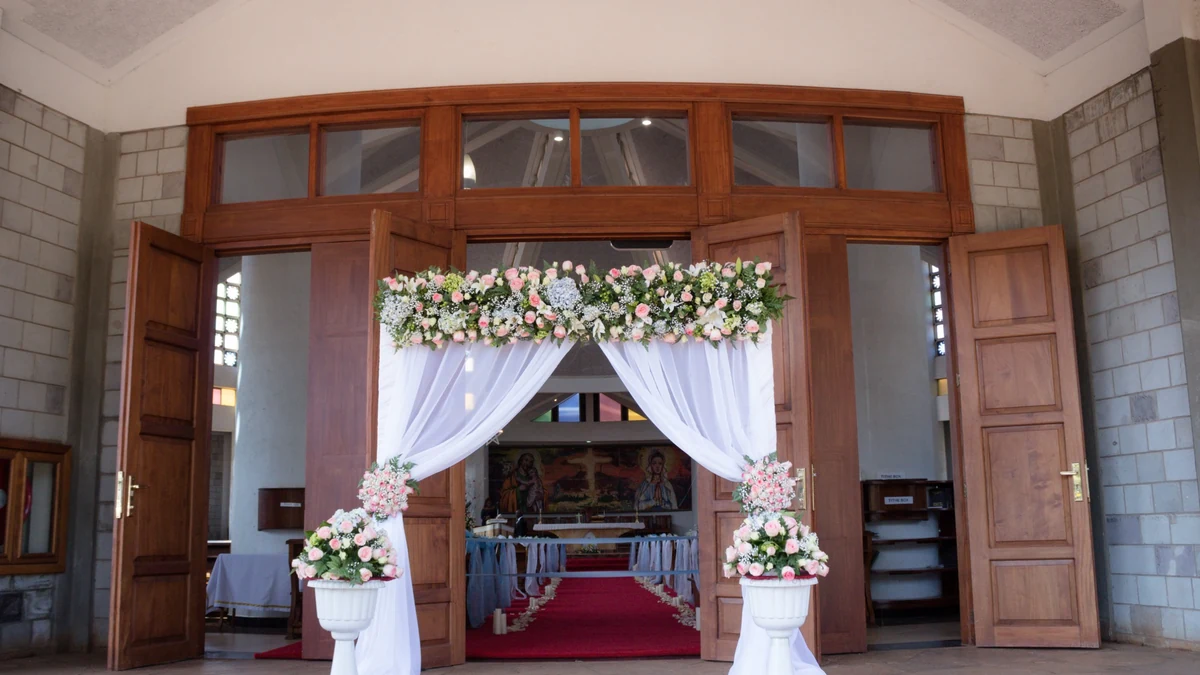 Decorated floral archway at the entrance of a church, looking down the red carpet aisle toward the altar before a wedding ceremony
