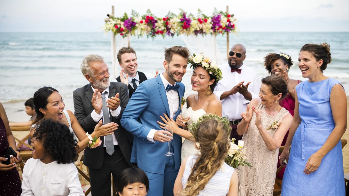 Wedding guests in light summer clothing toasting the couple at a beachfront ceremony