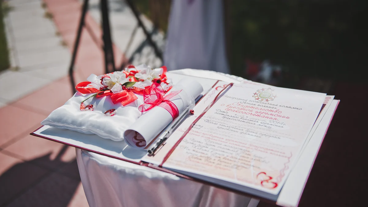 Wedding rings on a cushion beside an open ceremony register on a draped signing table