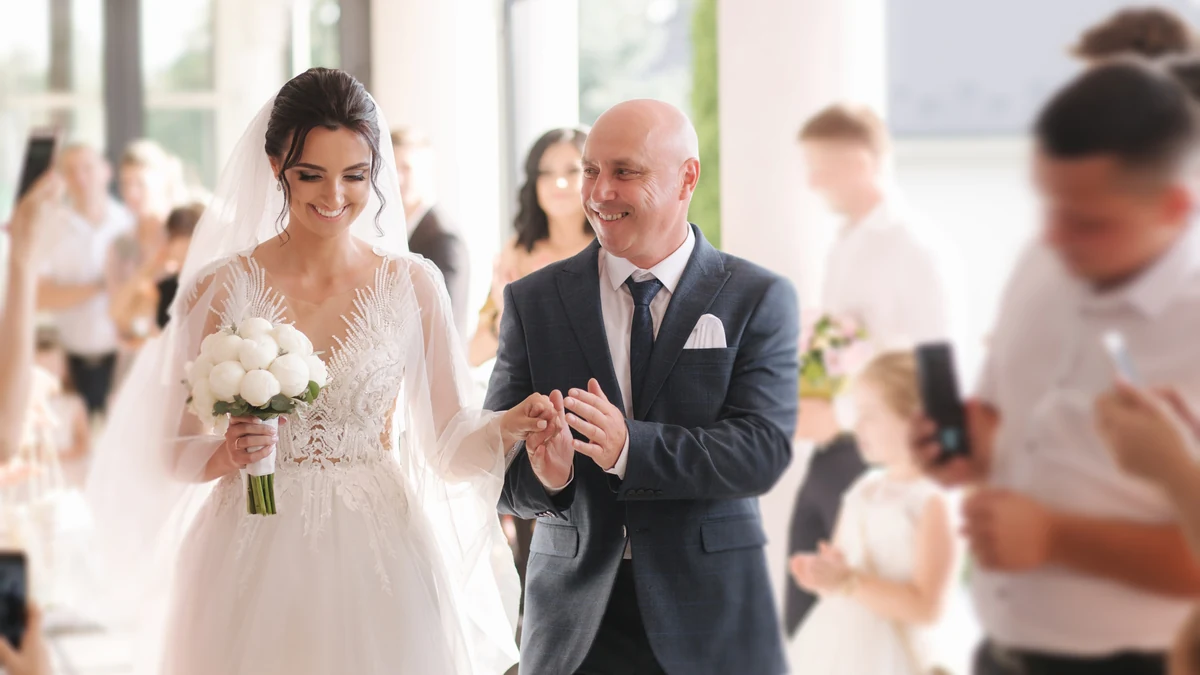 Bride walking down the aisle hand in hand with her father as guests look on, showing the traditional wedding processional order