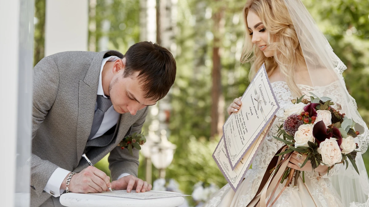 Groom signing the marriage document at a small table while the bride holds her certificate and bouquet