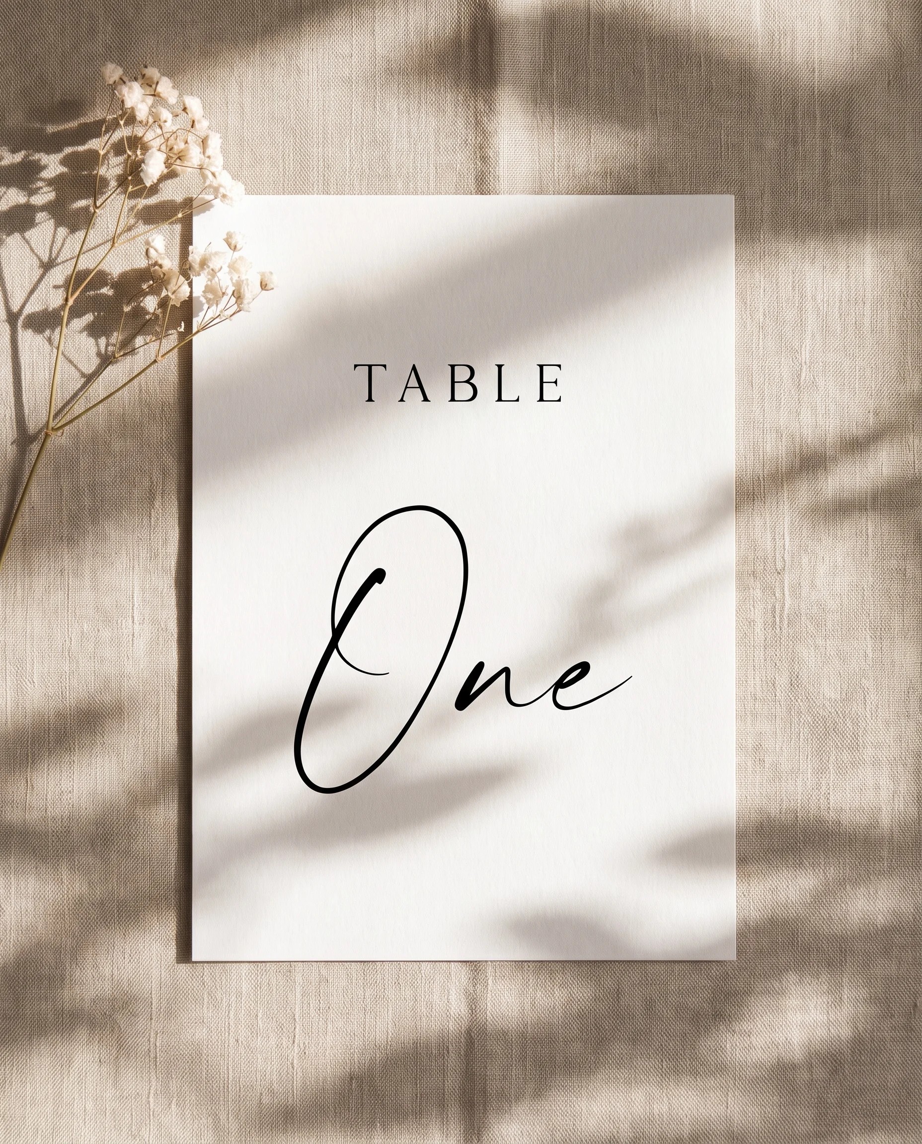 Sunlit wedding table number — single card lying flat under soft natural light with a slight overhead angle, wedding table numbers