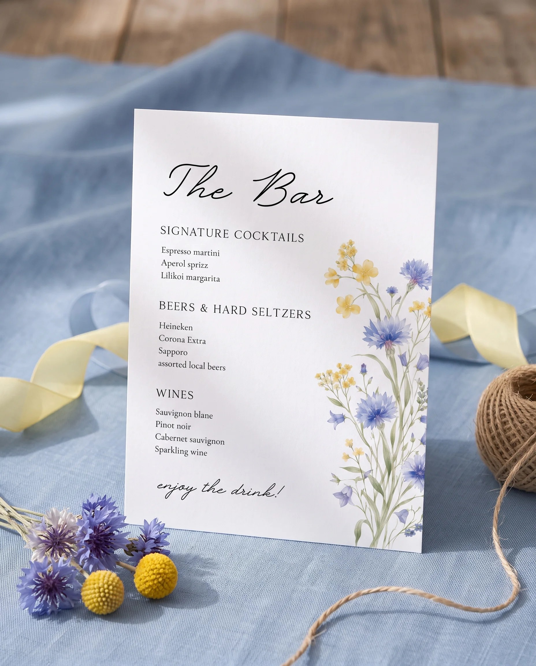 Cornflower — bar menu displayed upright on premium editorial paper under soft natural light at a slight overhead angle, wedding bar sign.