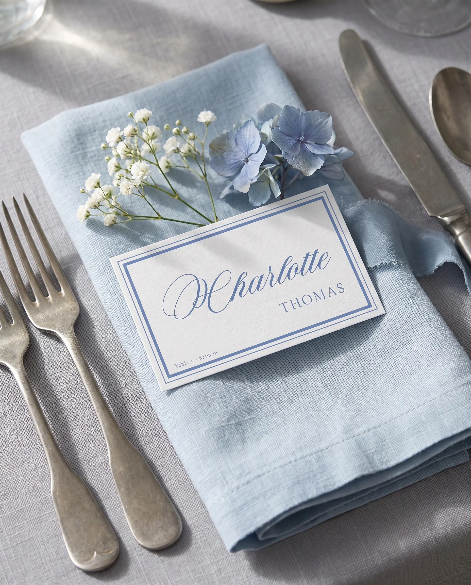 Azure Flourish wedding place cards — a single card at a set place setting under soft natural light, wedding name cards