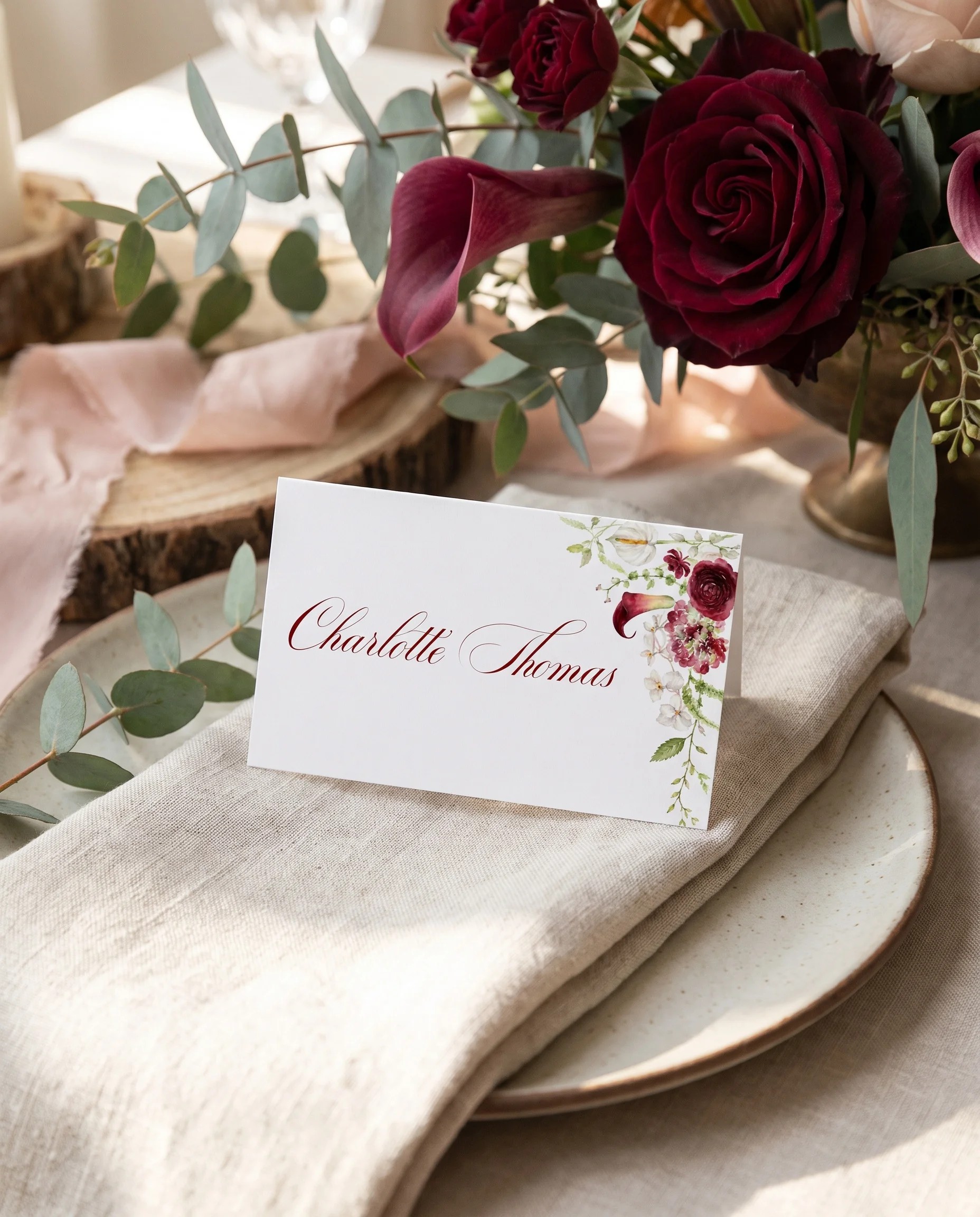 Burgundy Calla wedding place cards — a burgundy place card at a set place setting under soft overhead light, wedding name cards