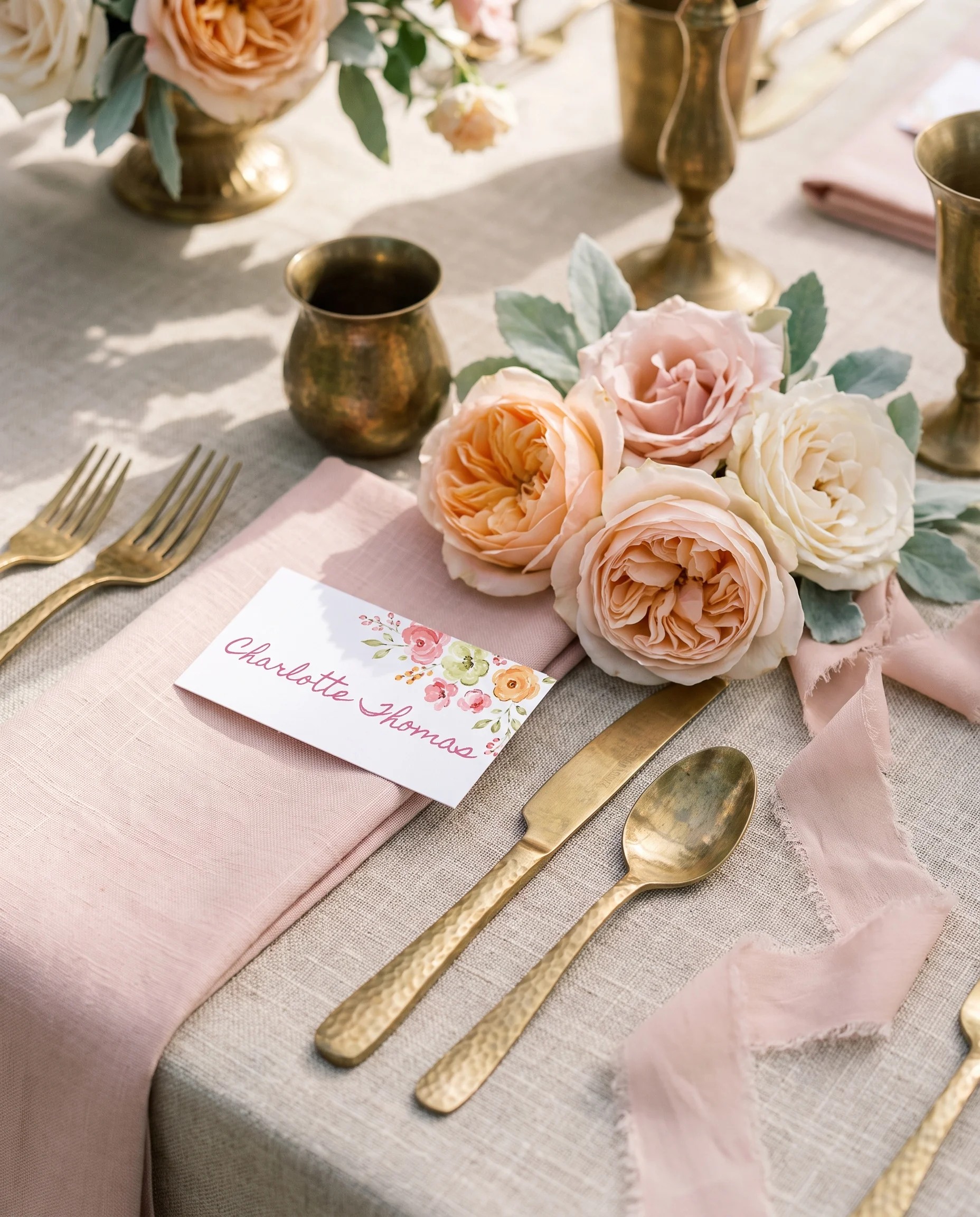 Blush garland wedding place cards — a single card shown at a set place setting under soft overhead light, wedding name cards.